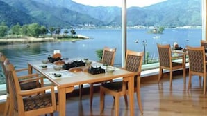 A dining area with a table and chairs, a view of a lake with mountains in the background. - Fuji Kawaguchiko Onsen Lakeland Hotel Mizunosato (Fujikawaguchiko)