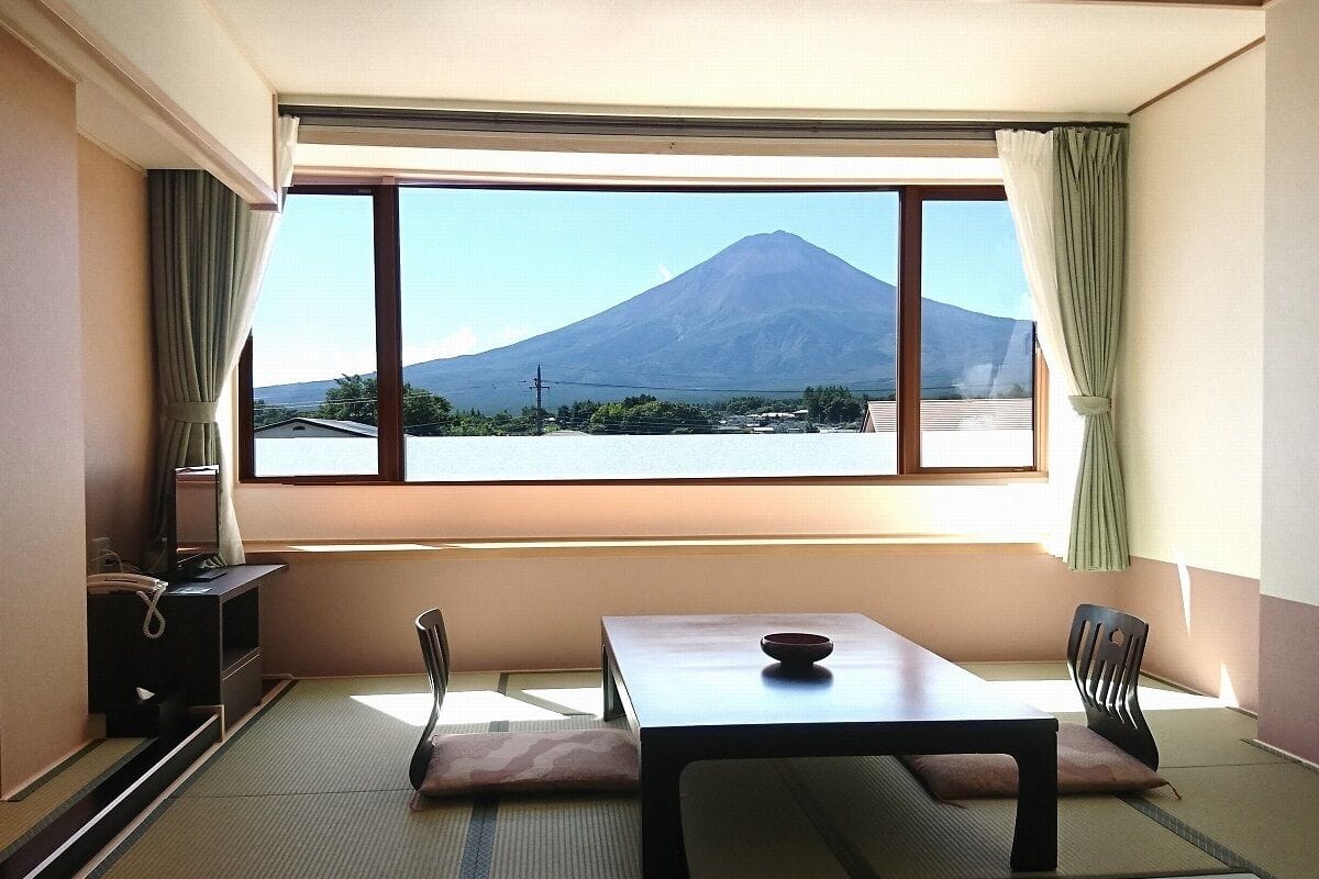 Ein Zimmer mit Tatami-Boden, einem niedrigen Tisch, einem Stuhl und Blick auf einen Berg.