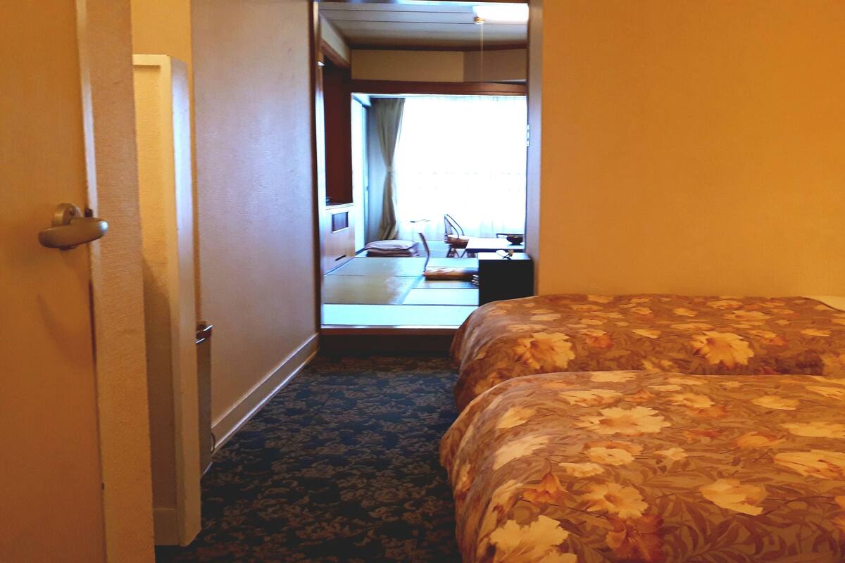 Ein Hotelzimmer mit Bett, kleinem Tisch, Stuhl und Blick ins Freie.