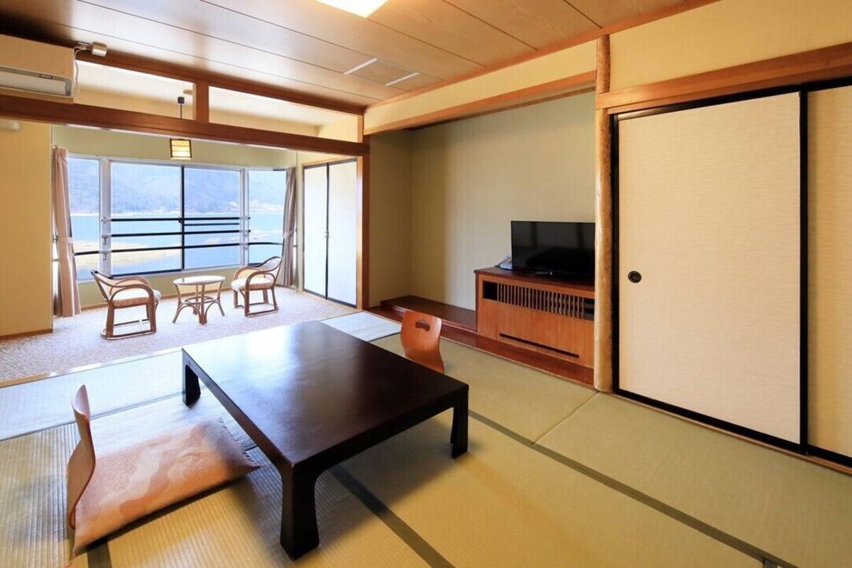Ein traditioneller japanischer Raum mit Tatami-Böden, einem niedrigen Tisch, einem Fernseher und einer Schiebetür.