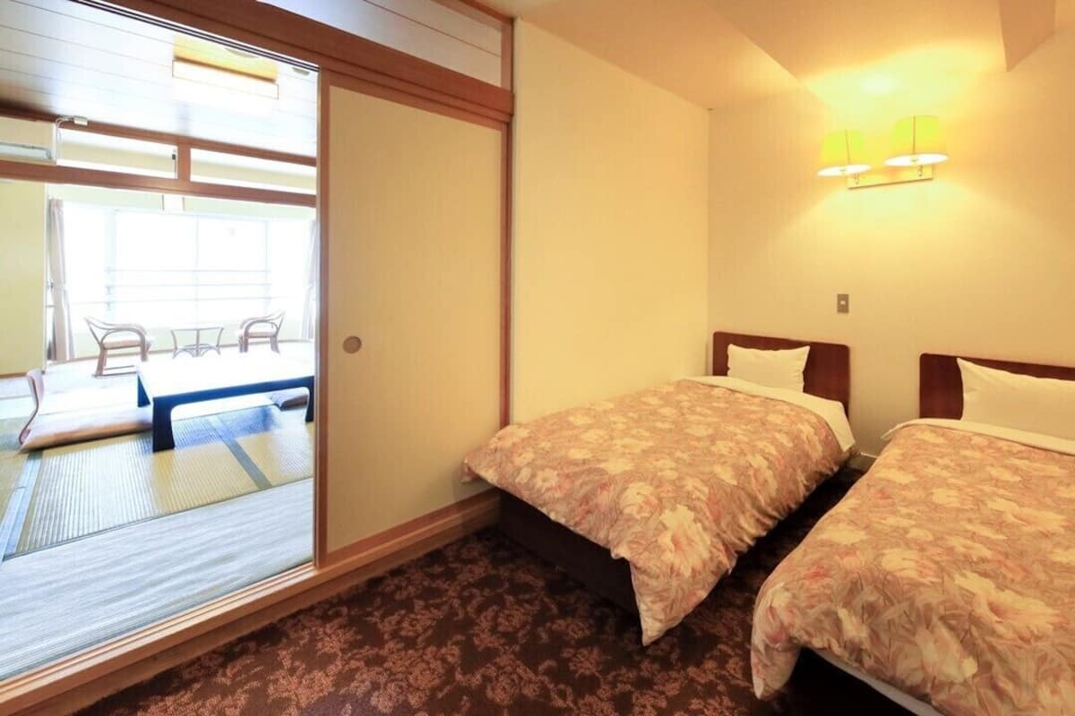 Ein Hotelzimmer mit zwei Betten, einer Schiebetür zu einem Balkon und einem kleinen Tisch mit Stühlen.