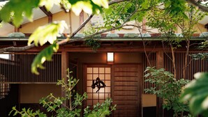 A traditional Japanese house with a wooden gate, a lantern, and lush greenery. - Oiwakeya Ryokan (Matsumoto)
