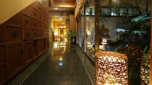 A hallway with wooden cabinets, a glass door with plants, and a woven light fixture. - Oiwakeya Ryokan (Matsumoto)