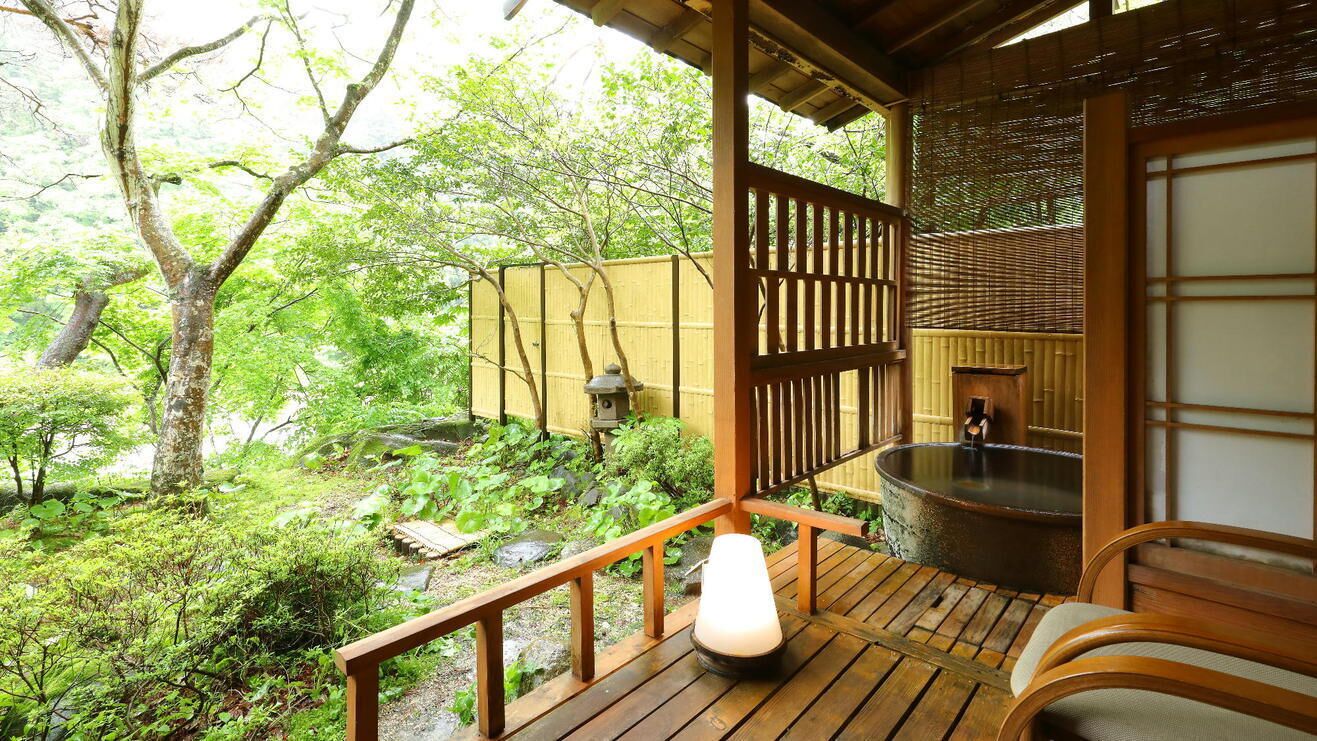 Une terrasse en bois avec une source d’eau chaude, une lanterne et une pièce de style japonais traditionnel.