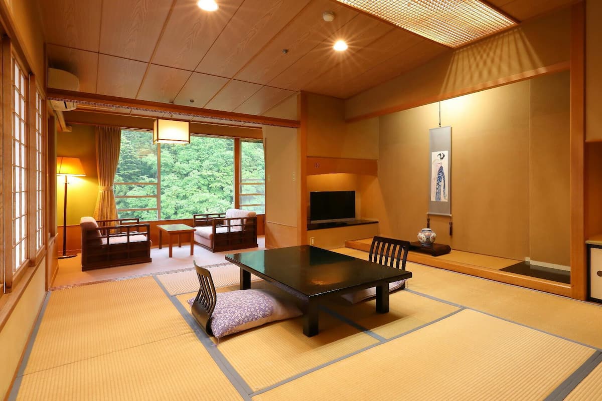 Une pièce de style japonais traditionnel, avec un sol recouvert de tatamis, une table basse, des chaises, un téléviseur et des œuvres d’art accrochées aux murs.