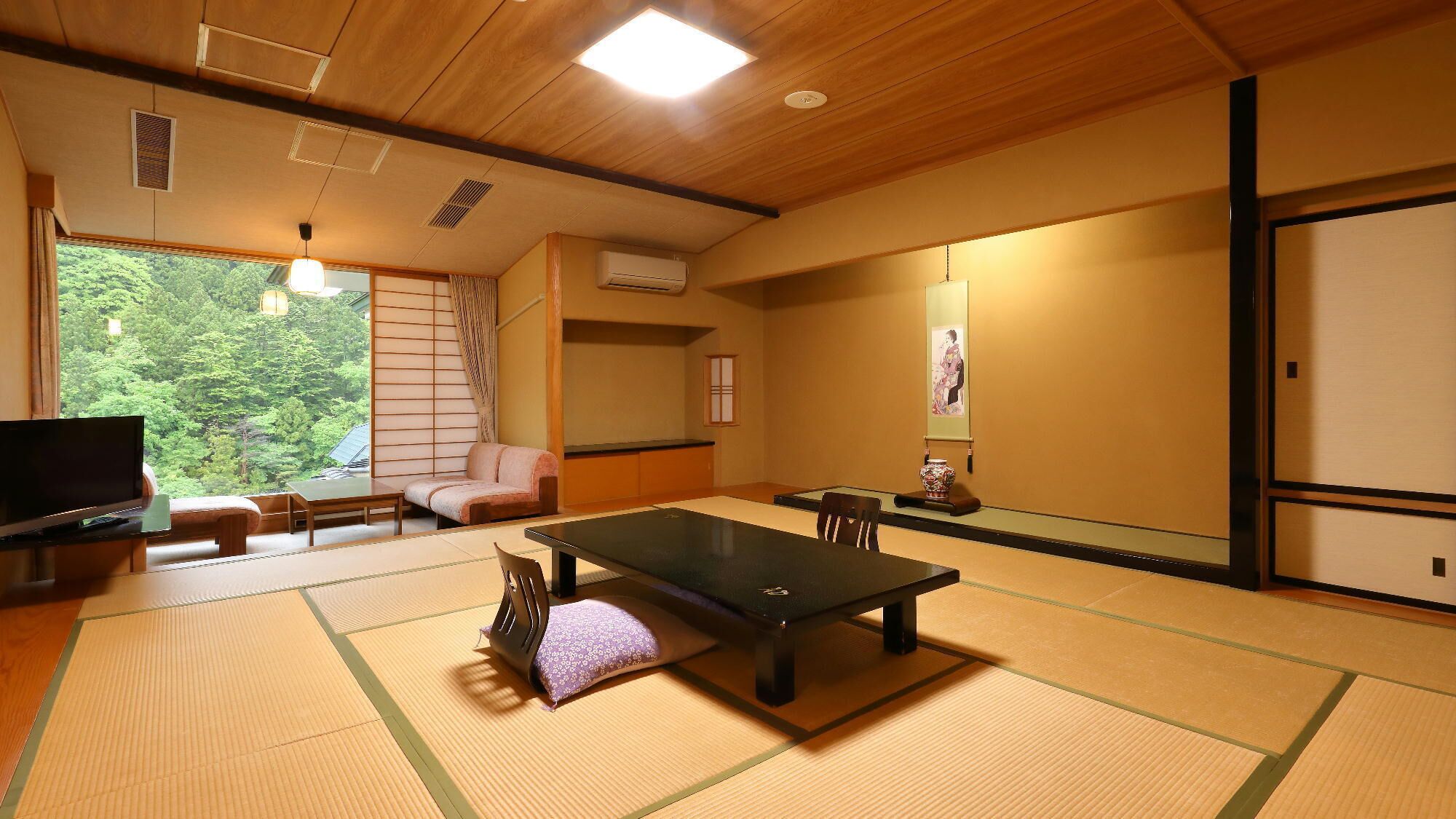 Une pièce avec un sol recouvert de tatamis, comprenant une table en tatami, un canapé, un téléviseur et une porte coulissante donnant sur un paysage verdoyant.