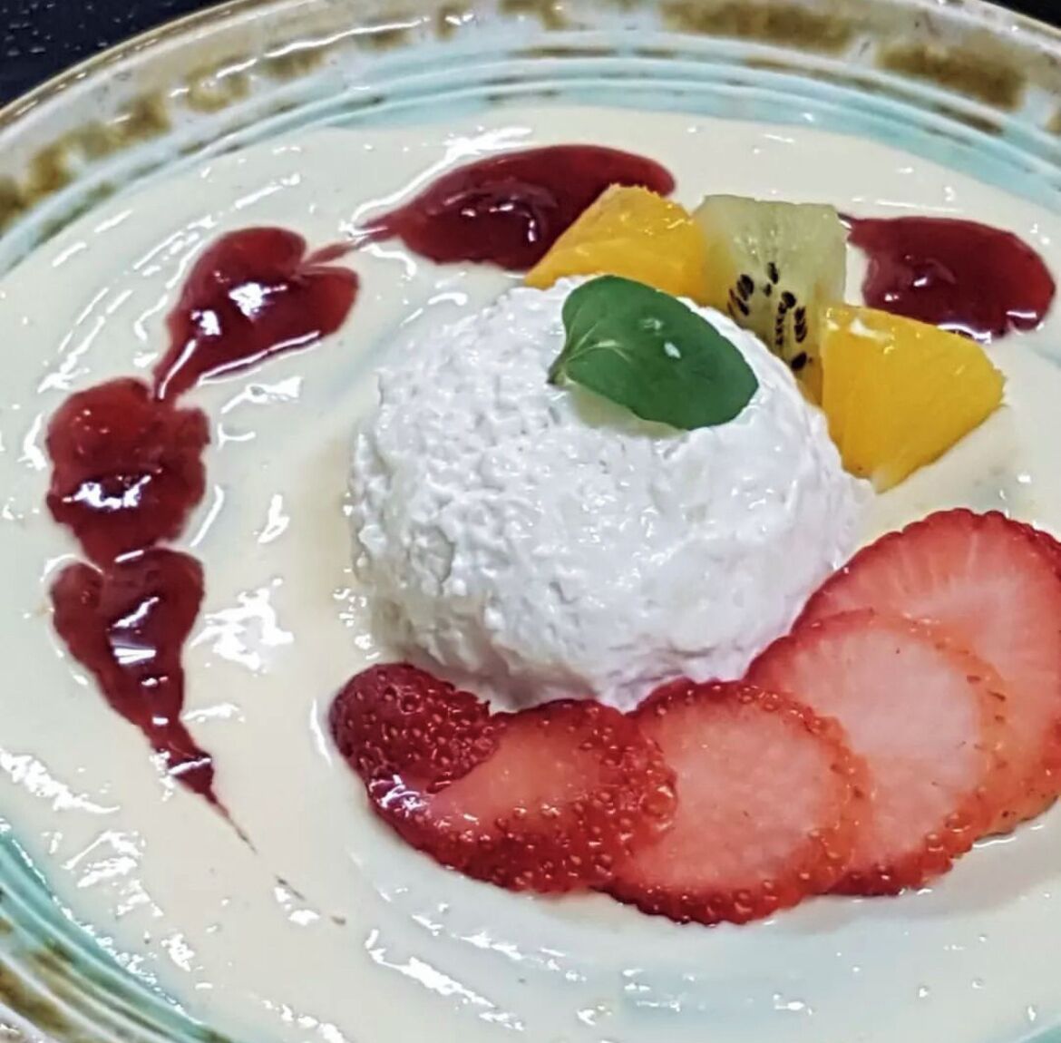 A dessert with white cream, strawberries, kiwi, and mango slices on a plate.