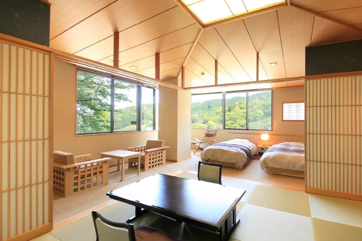 A traditional Japanese-style room with tatami flooring, a low table, and a bed with a view of the forest.