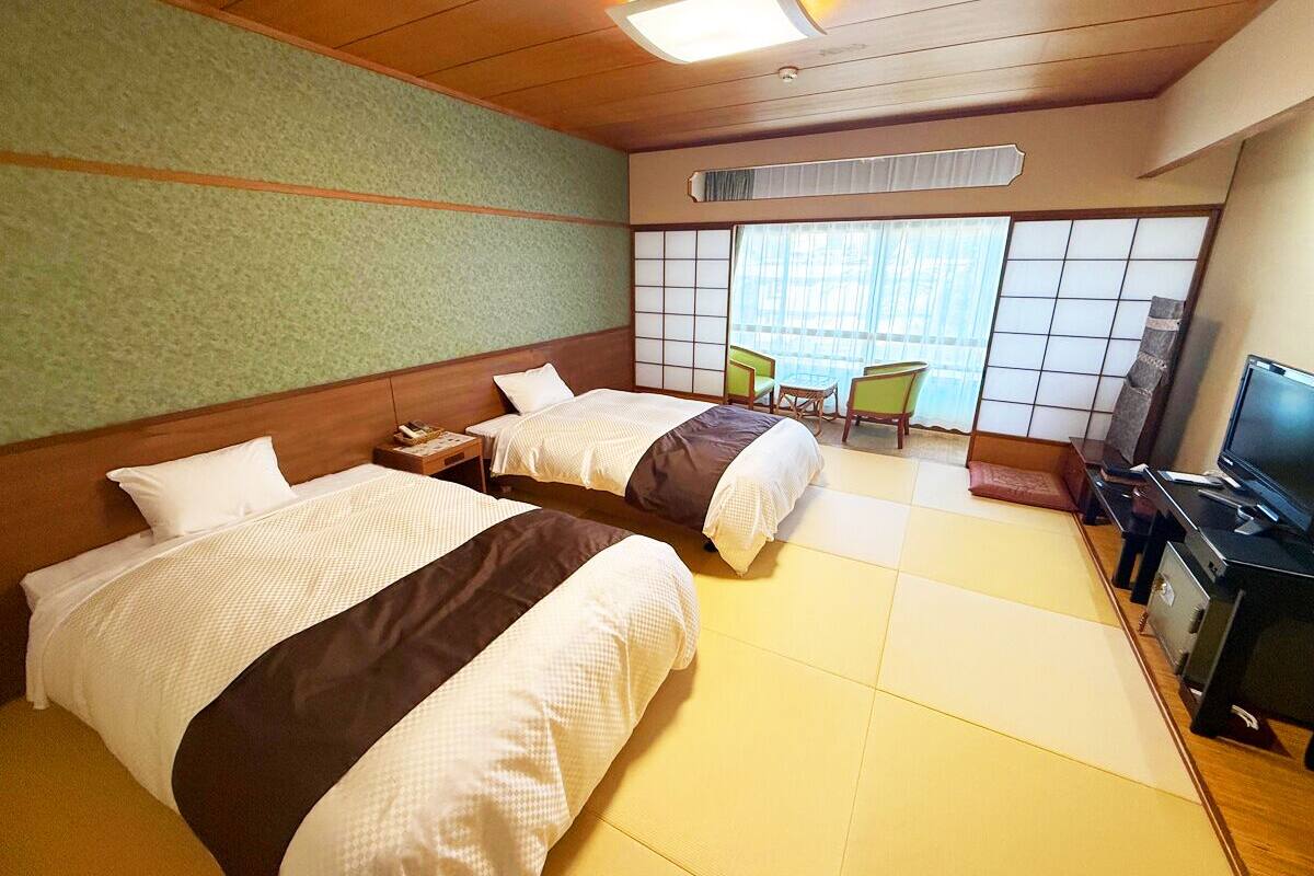 A hotel room with two beds, a television, a desk, and a view of the outside through a window with a view of the sky.