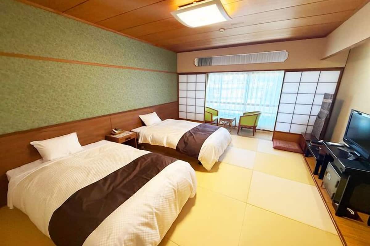 A hotel room with two beds, a TV, a desk, and a view of the outside through large windows.