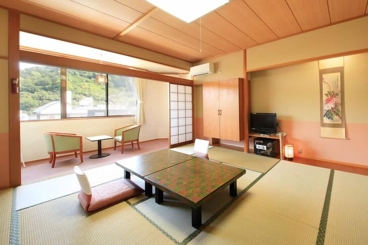 A traditional Japanese room with tatami flooring, a low table, chairs, a TV, and a sliding door.