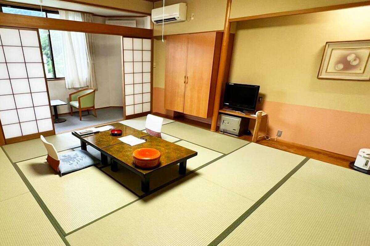 Une pièce de style japonais traditionnel, avec un sol recouvert de tatamis, une table basse, un téléviseur et des portes coulissantes.