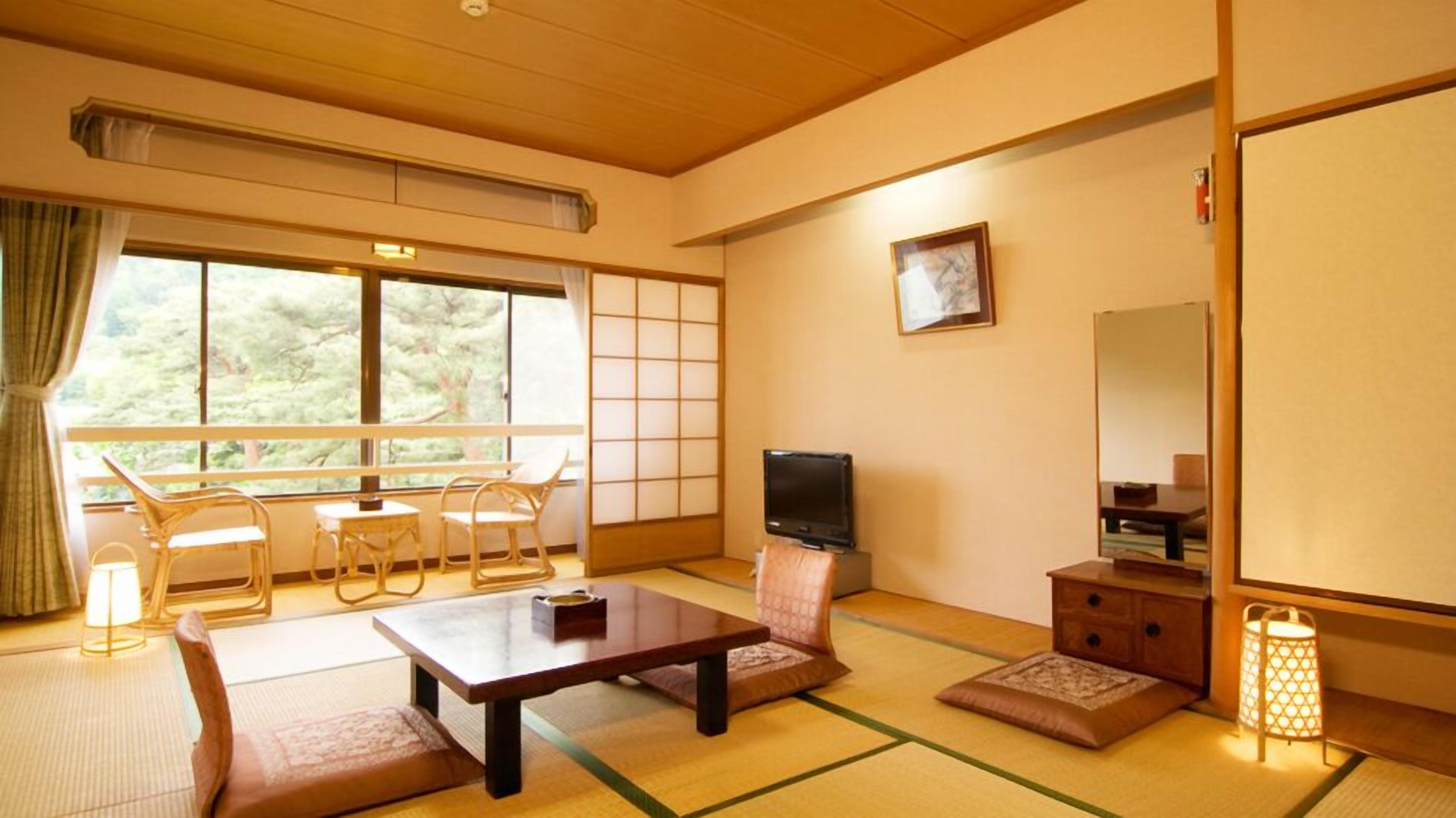 A traditional Japanese-style room with tatami flooring, a low table, a television, and a sliding door.