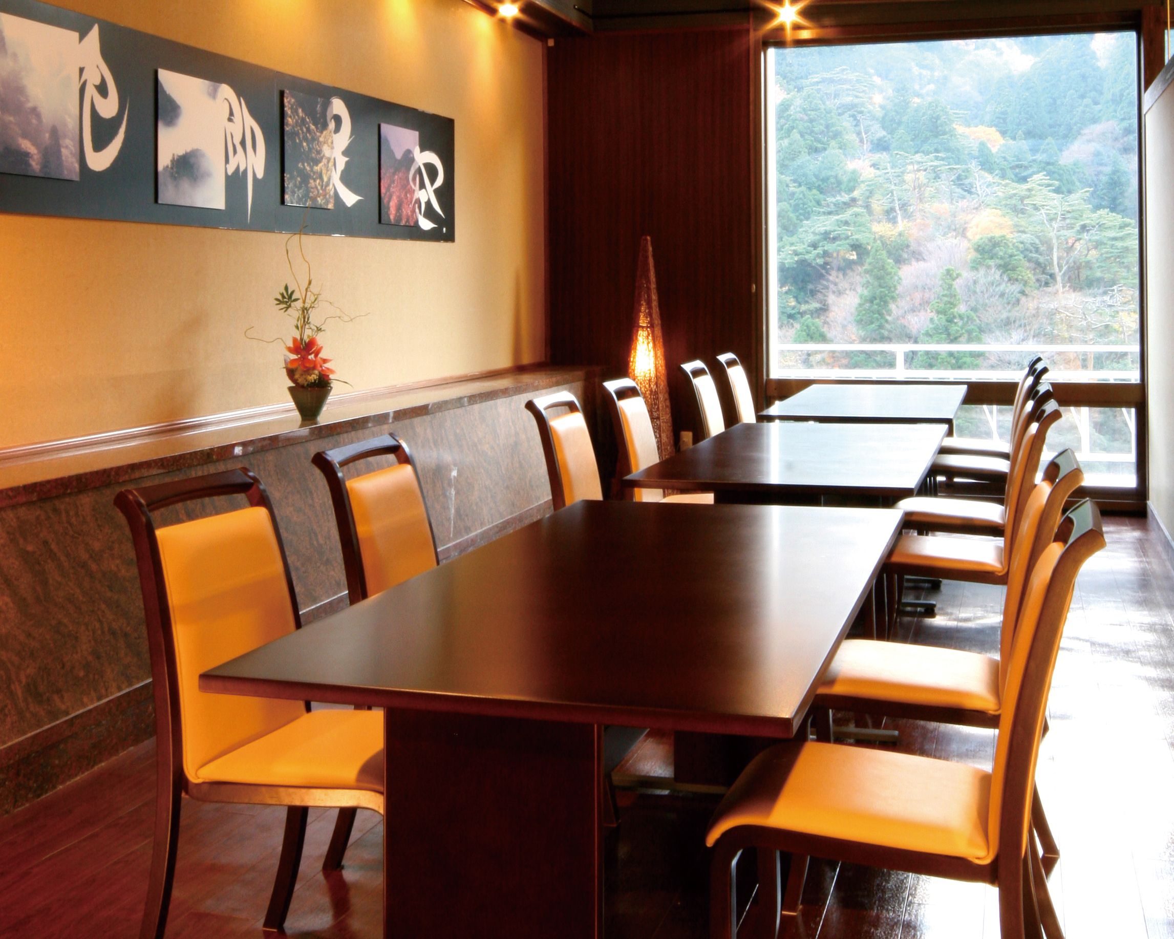 A conference room with a long table and multiple chairs, a potted plant, and a window with a view of a forest.