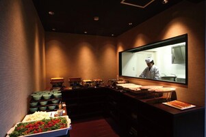 Una zona de cocina con un chef en el reflejo, una mesa de buffet con comida y equipamiento de cocina.