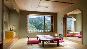 Una habitación japonesa tradicional con suelo de tatami, una mesa baja y vistas a una montaña boscosa.