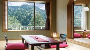 Una habitación tradicional japonesa con suelo de tatami, una mesa baja y vistas a una montaña boscosa.