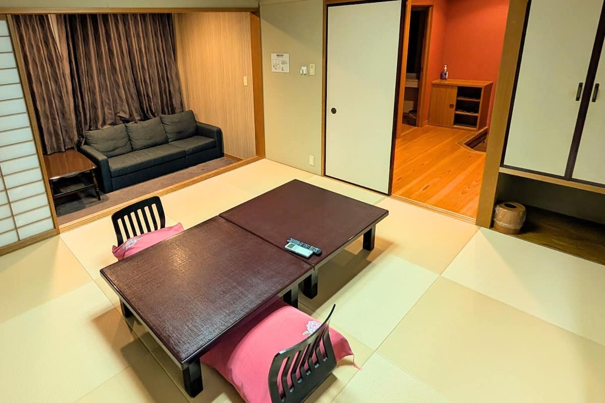 Una habitación japonesa tradicional con esteras de tatami, una mesa baja, sillas y un futón.