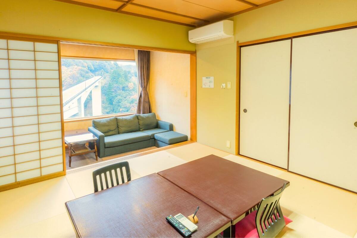 Una habitación con puerta corrediza, un sofá, una mesa con sillas y vistas a un puente y árboles.