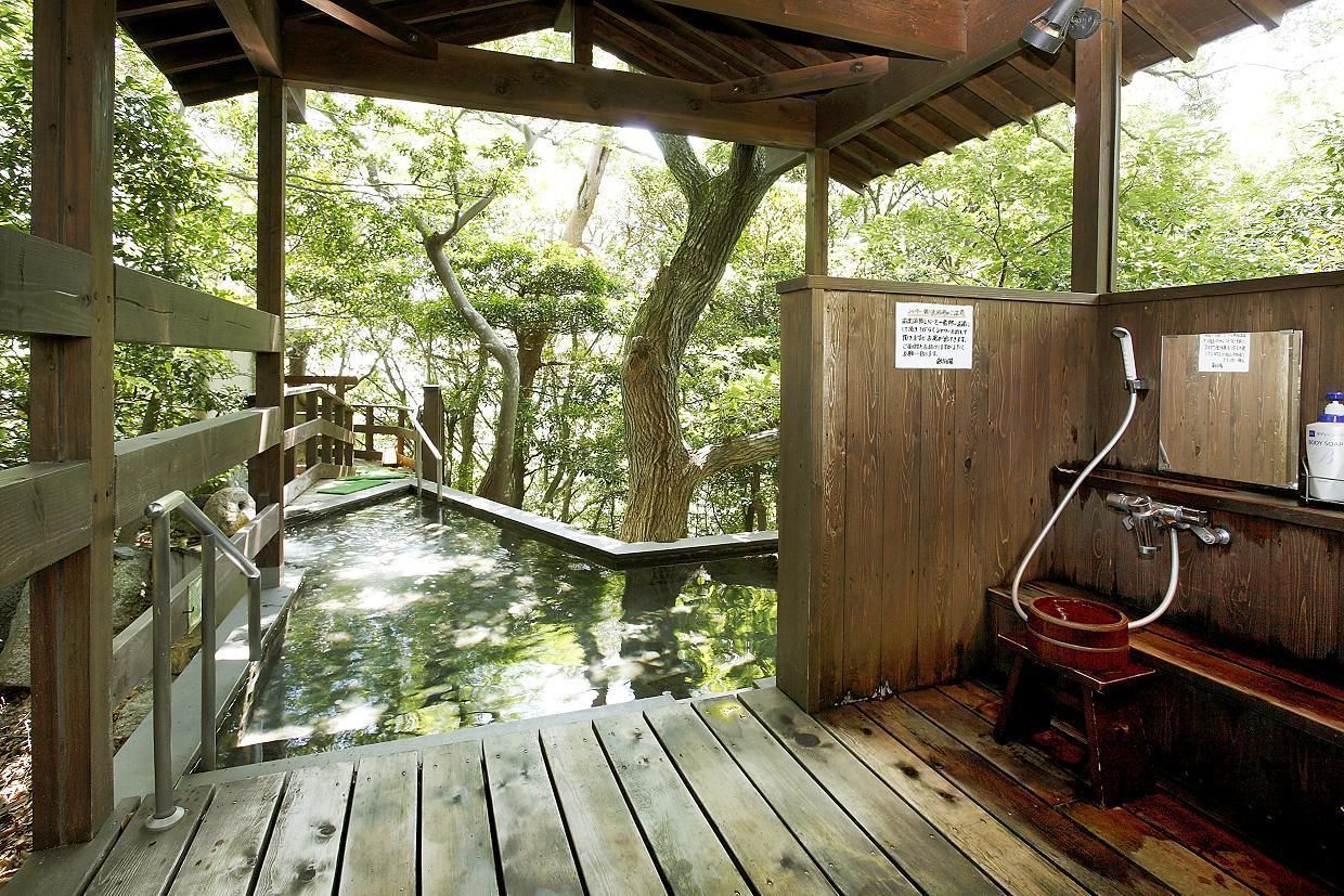 A wooden outdoor hot spring area with a wooden deck, a small wooden bench, and a hot spring with a wooden seat.