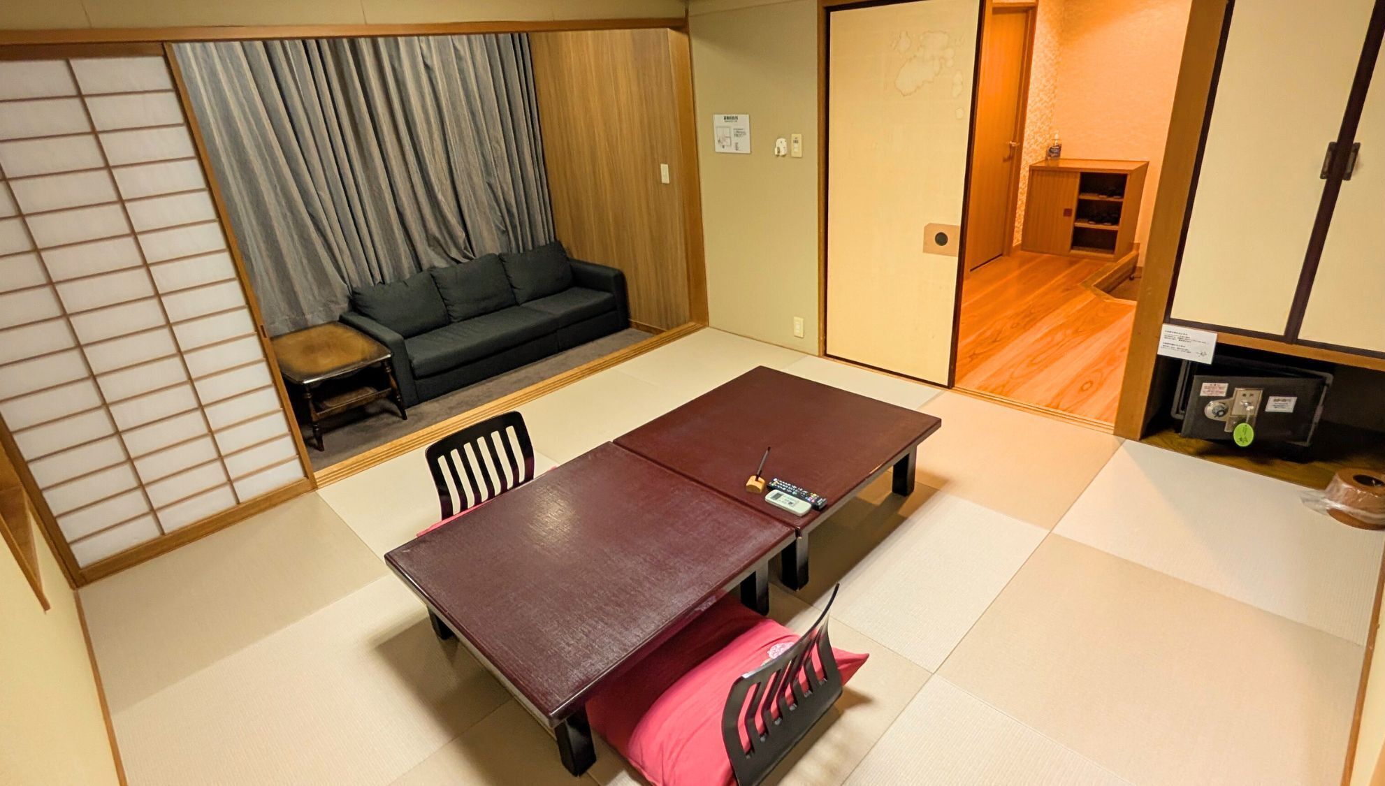 Una tradizionale stanza giapponese con pavimento in tatami, un tavolino con cuscino, una poltrona e una porta scorrevole che dà su un'altra stanza.