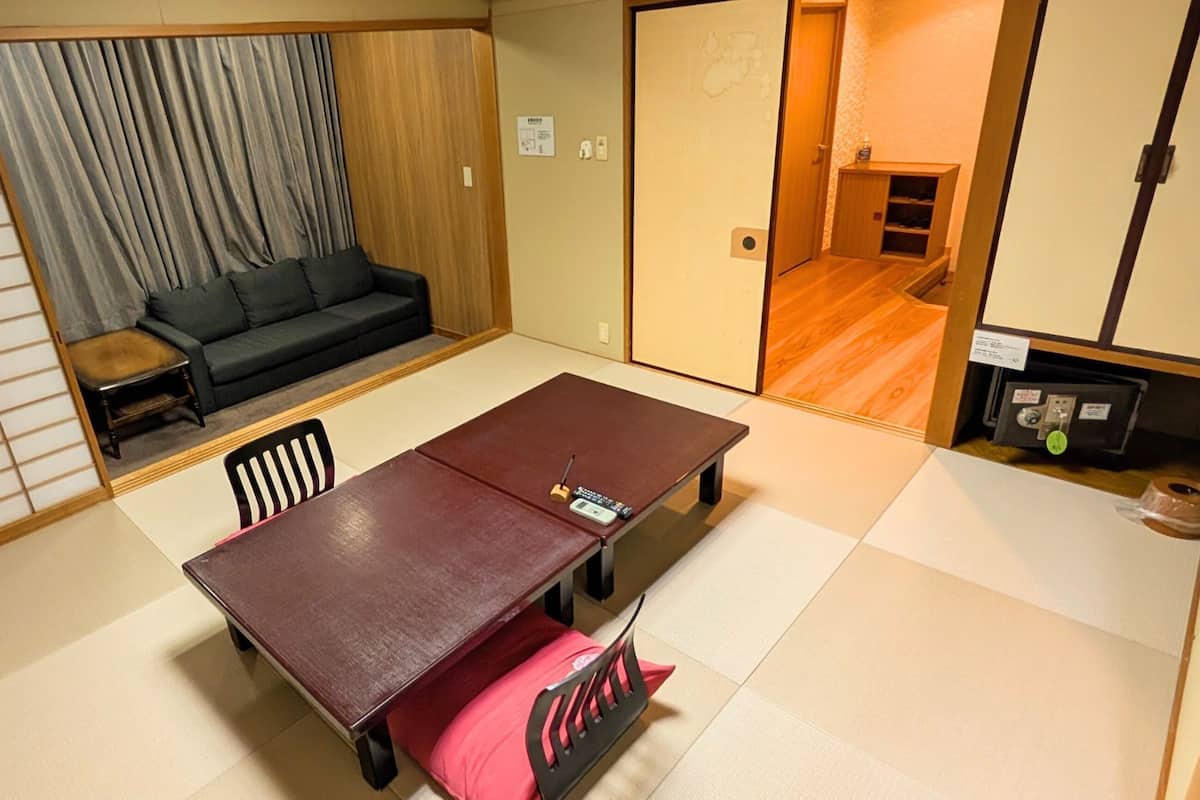 Una habitación japonesa tradicional con suelo de tatami, una mesa baja con cojín, un sofá y una puerta corredera que da a otra habitación.