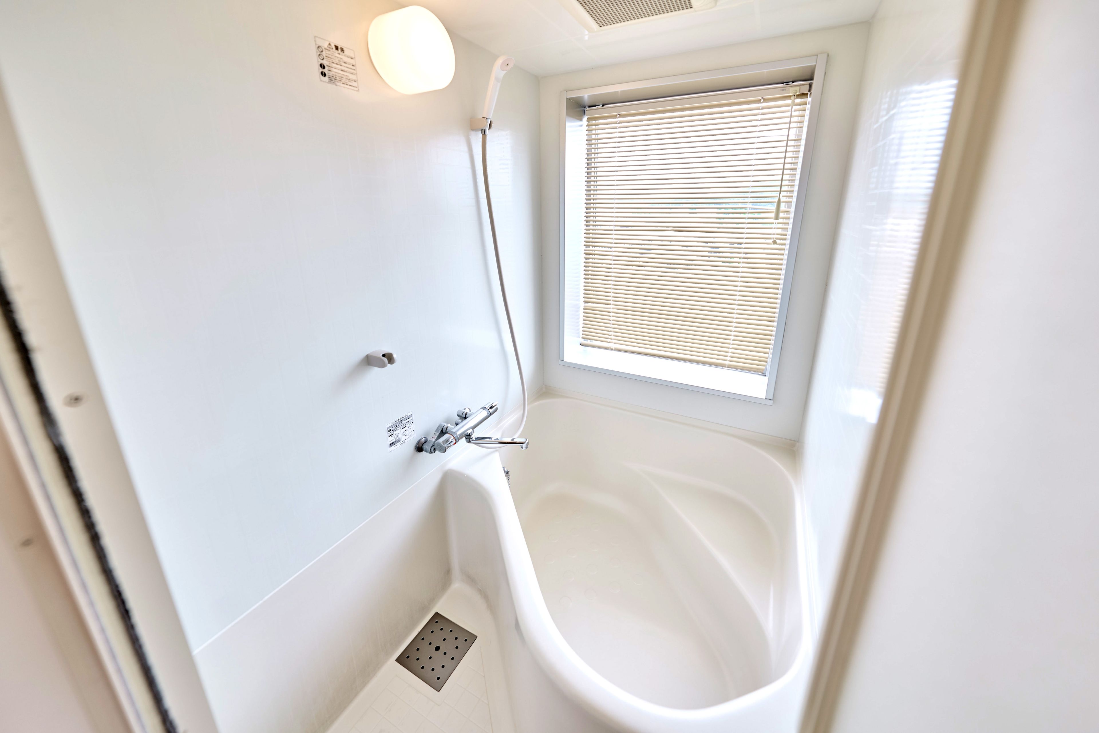 Un baño con bañera, ducha y ventana con persianas.