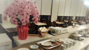A buffet setup with various dishes and utensils, a vase of pink flowers, and a counter with a cash register. - Smile Hotel Shirakawa (Nishigo)