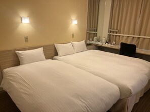 A hotel room with two beds, a desk with a chair, a mirror, and two wall-mounted lights.