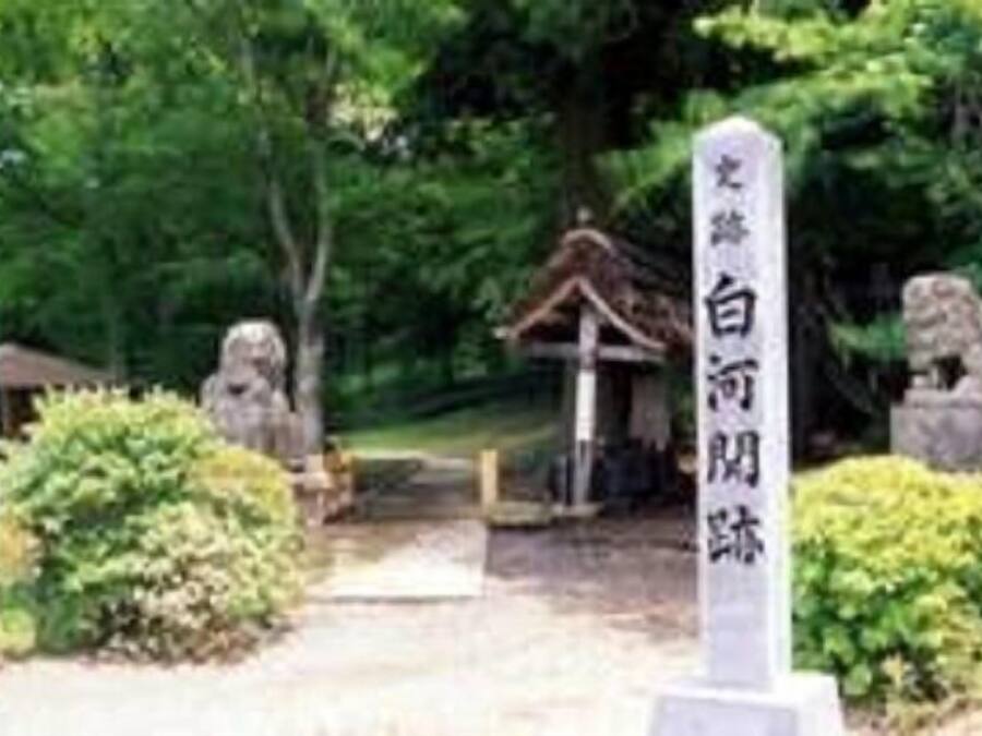 Um tradicional portão torii japonês que dá acesso a um santuário, rodeado por vegetação exuberante e lanternas de pedra.