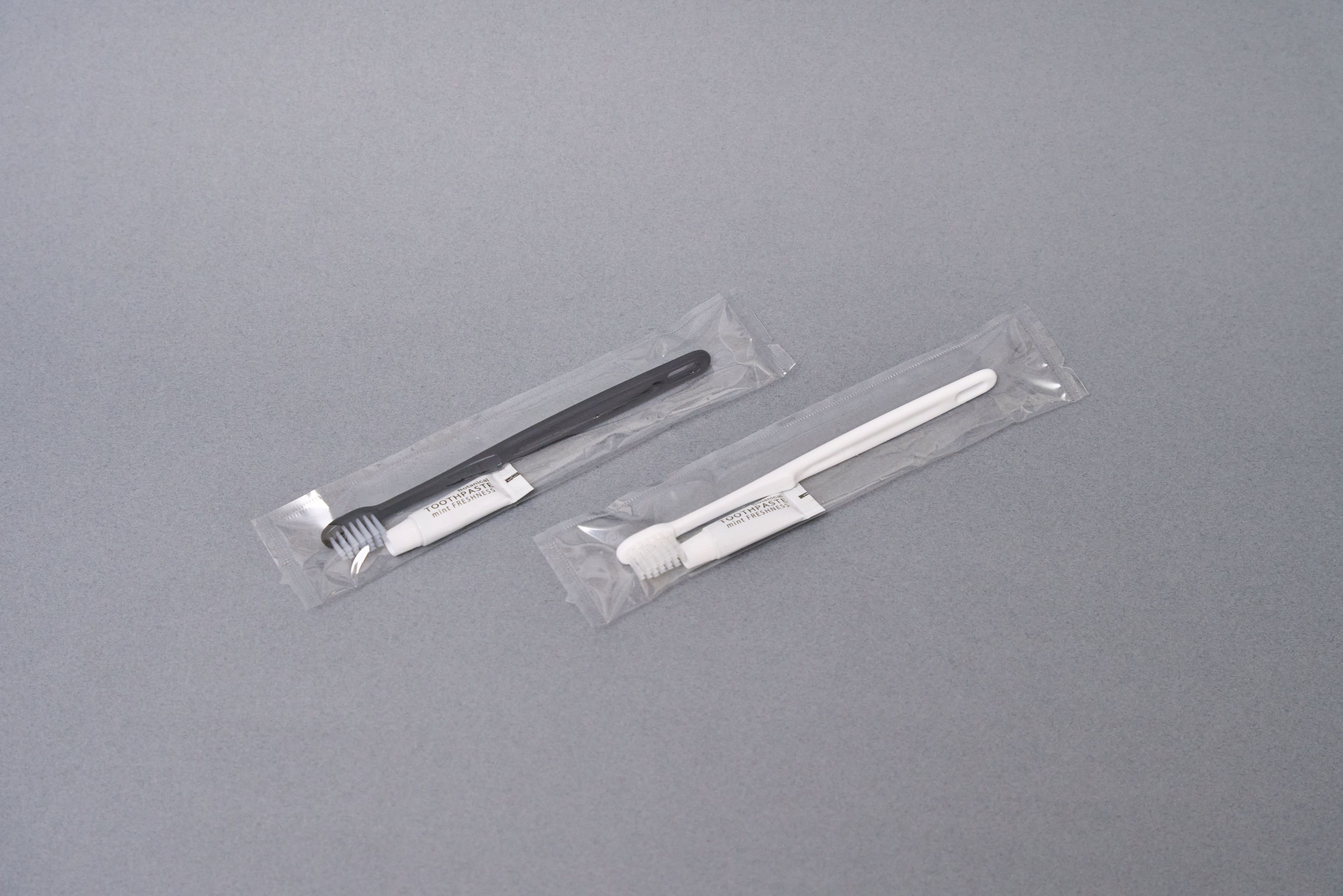Two toothbrushes in clear plastic packaging on a grey surface.