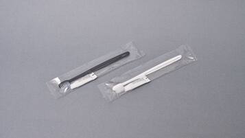 Two toothbrushes in clear plastic packaging on a grey surface.