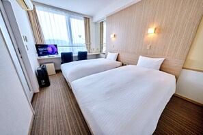 A hotel room with two beds, a desk, a television, and a window with curtains.