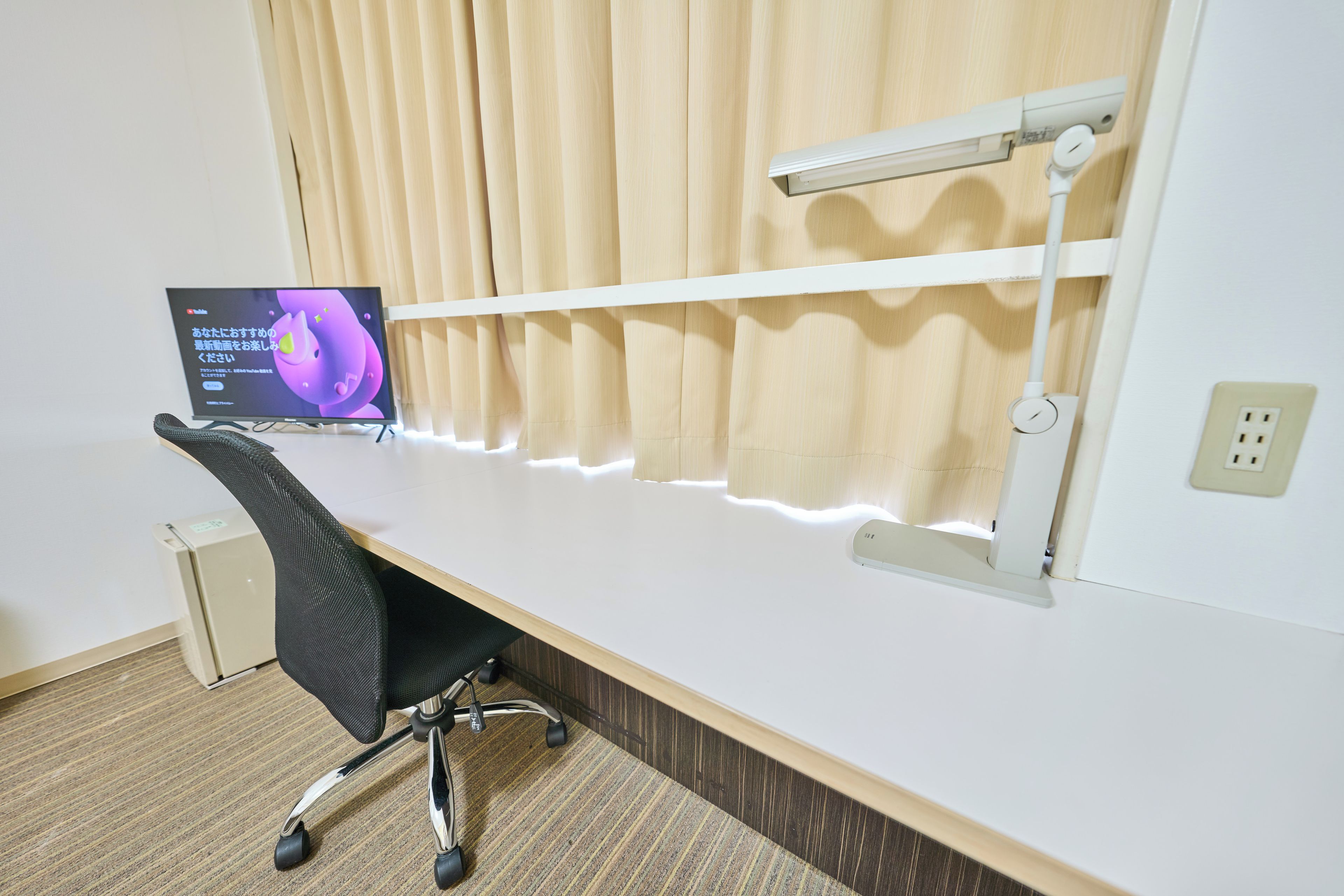 A modern office desk with a computer monitor, a chair, and a window with blinds.