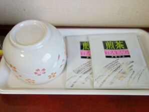 A ceramic teapot with floral patterns and two tea bags on a tray. - Hotel Green Pacific (Sendai)