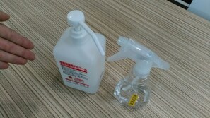 A white plastic bottle with a pump nozzle and a smaller plastic spray bottle with a yellow label on a wooden surface. - Hotel Green Pacific (Sendai)