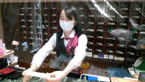 A person seated at a desk with a computer, surrounded by shelves with various items. - Hotel Green Pacific (Sendai)