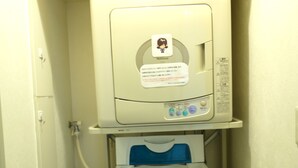 A compact, wall-mounted laundry machine with a control panel and a hanging clothes rack below it. - Hotel Green Pacific (Sendai)