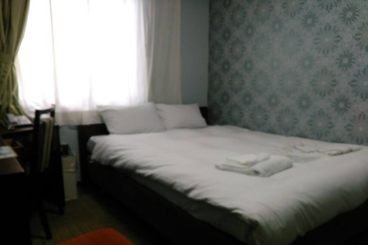Una cama individual con ropa de cama blanca, una silla y un escritorio en una habitación con papel tapiz estampado.