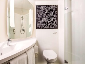 A bathroom with a white sink, a toilet, a shower, and a wall-mounted mirror. - Ibis London Wembley (London)