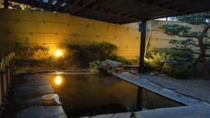 Uma área de piscina ao ar livre tranquila, com piso de pedra, pérgola de madeira e cerca de bambu.
