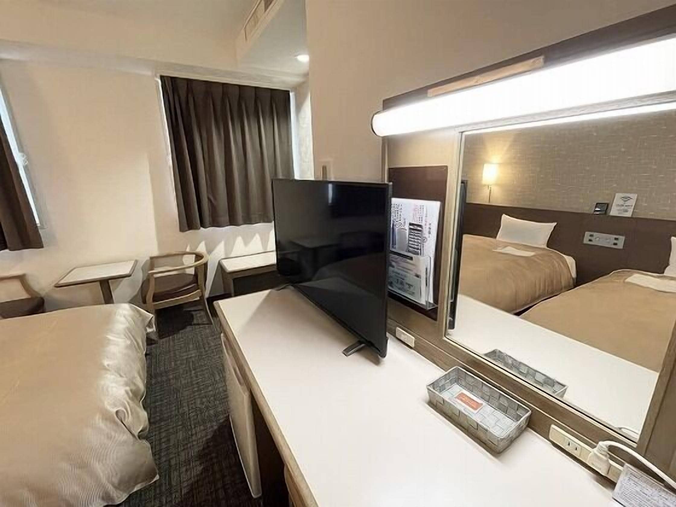 A hotel room with a bed, a desk, a chair, a television, and a mirror.