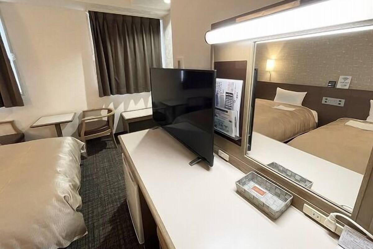 A hotel room with a bed, a desk, a chair, a television, and a mirror.