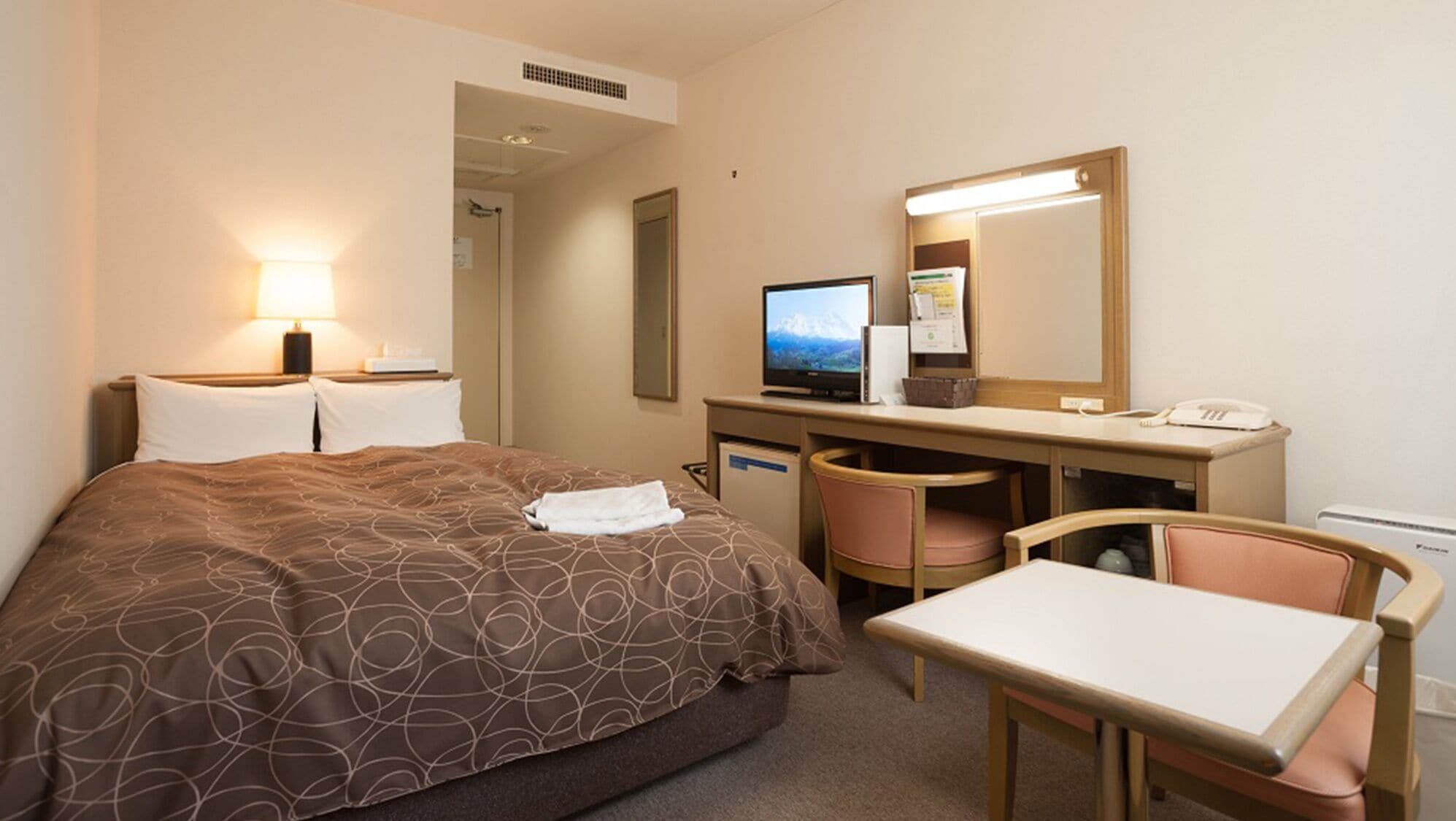 A hotel room with a bed, desk, chair, computer, and a telephone.