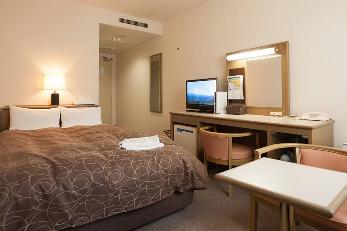 A hotel room with a bed, desk, chair, computer, and a telephone.