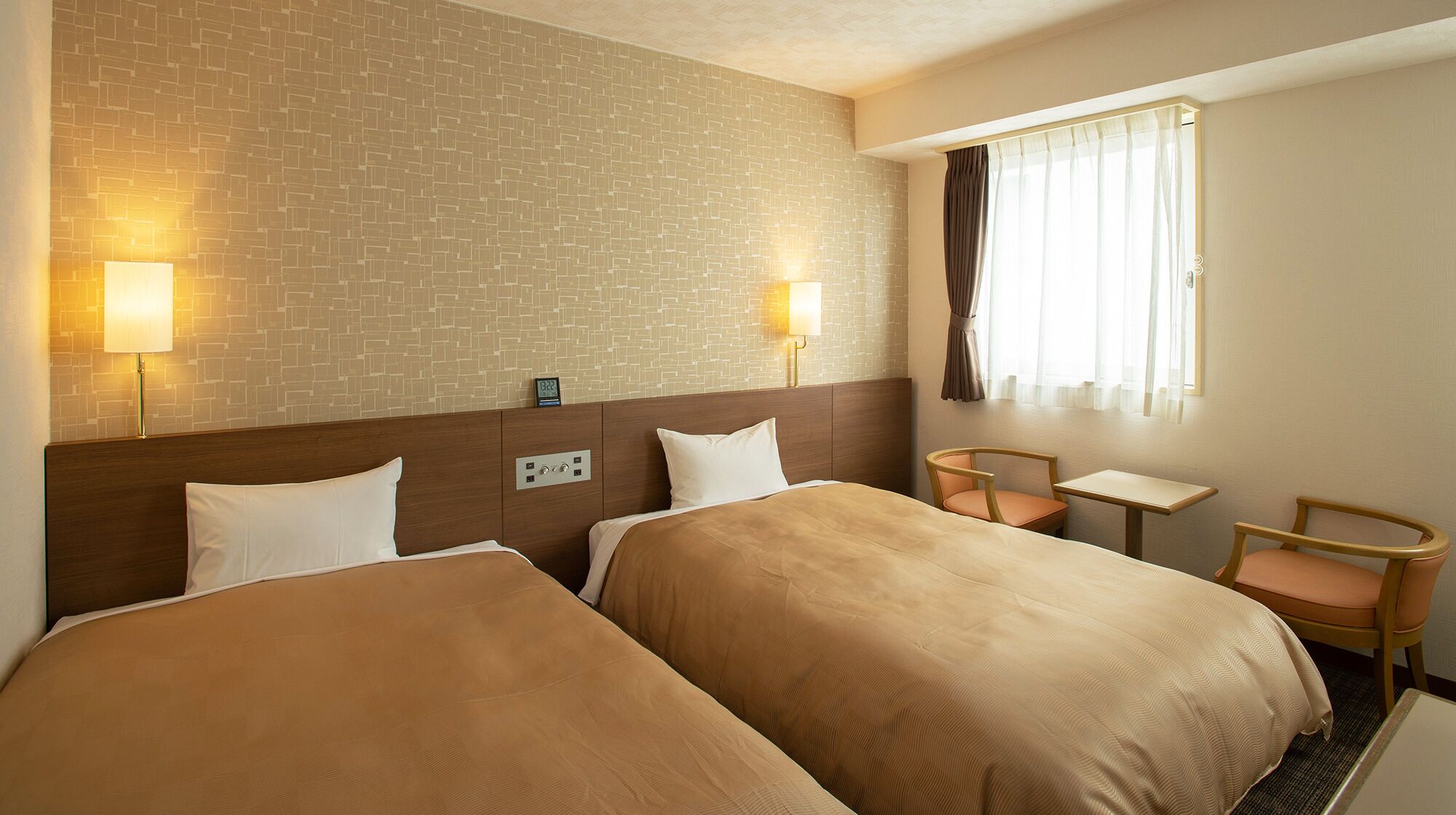 A hotel room with two beds, a small table, two chairs, a clock, and a window with curtains.