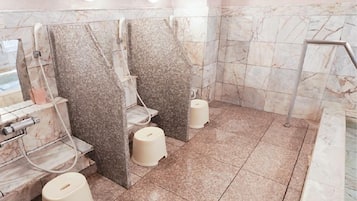 Baño público con paredes y pisos de mármol, lavamanos individuales y inodoros con escalón.