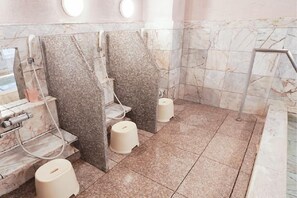Baño público con paredes y pisos de mármol, lavamanos individuales y inodoros con escalón.