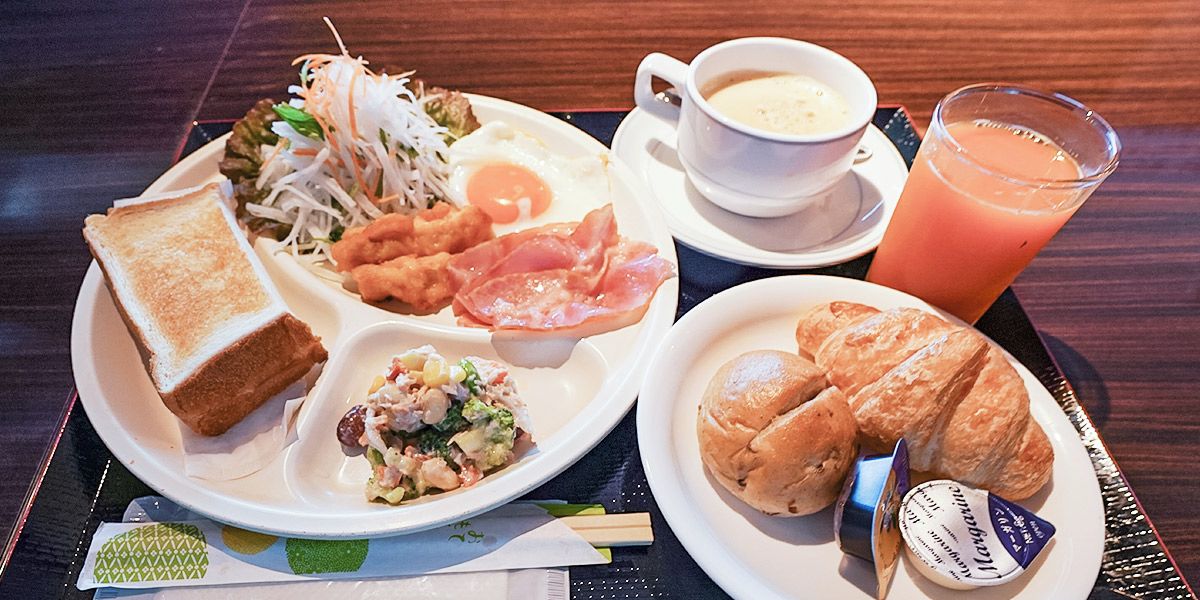 A breakfast tray with toast, eggs, bacon, a croissant, and a glass of orange juice.