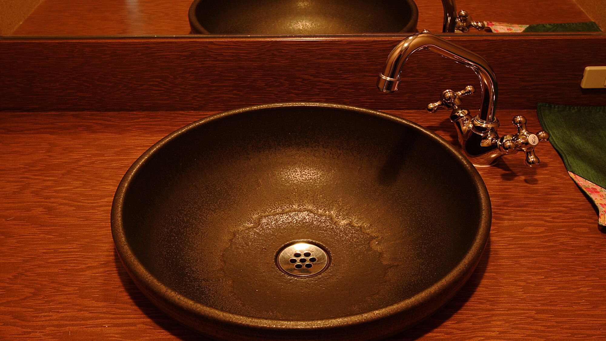 A round, dark-colored sink with a single drain, a faucet with a curved spout, and a mirror above it.